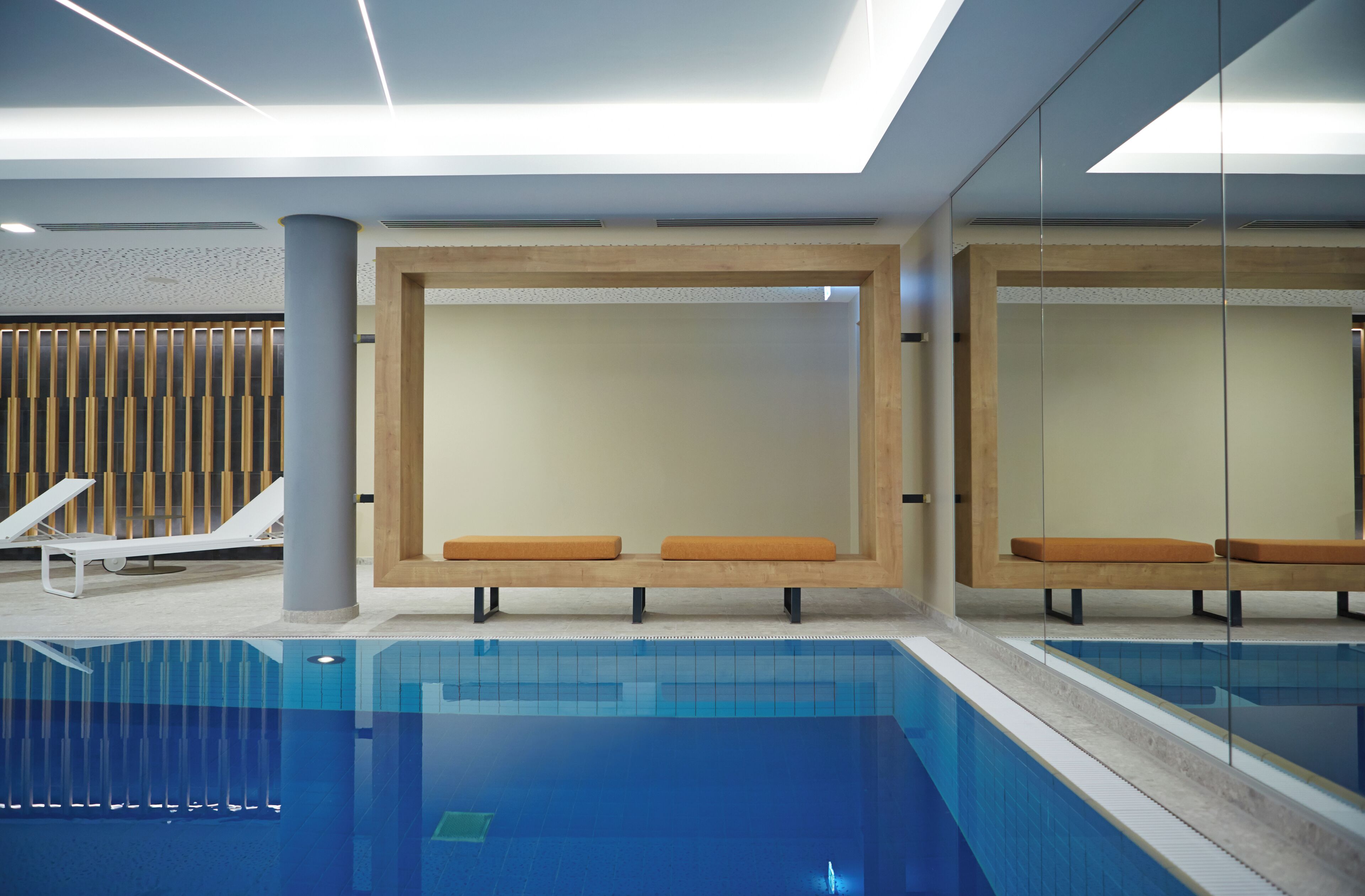 A modern indoor pool area with lounge chairs and benches.