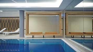 A modern indoor pool area with lounge chairs and benches.