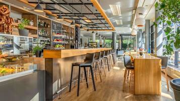 Un espace bar moderne avec un comptoir en bois, des tabourets de bar et une variété de boissons et d’en-cas.