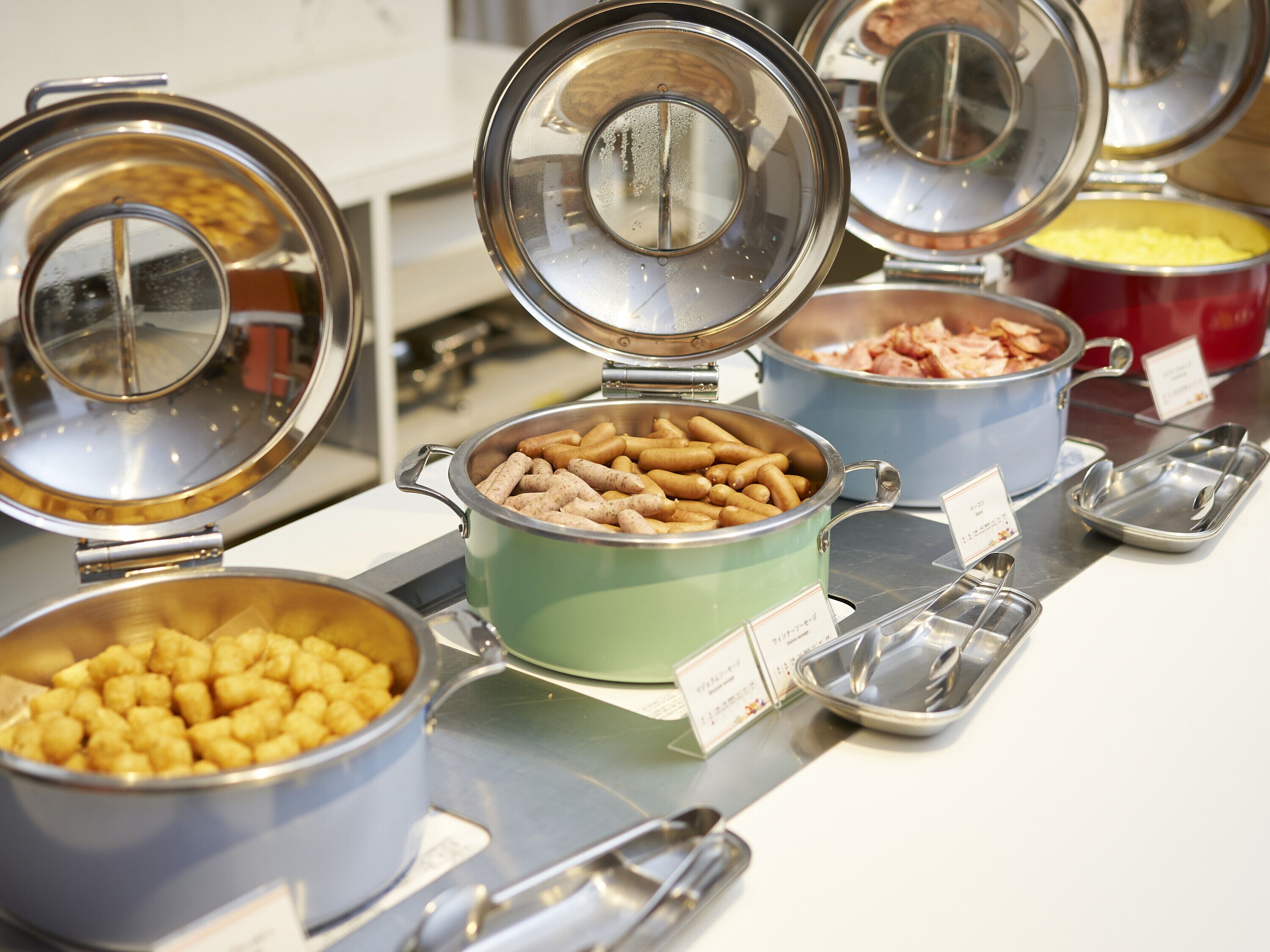 Un buffet con diversi cibi esposti in pentole e ciotole, tra cui salsicce e crocchette di patate.
