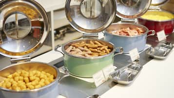 Un buffet proposant divers plats servis dans des récipients et des bols, notamment des saucisses et des pommes de terre en forme de petits cubes.