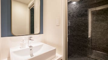 A bathroom with a white sink, a mirror, and a shower with dark marble walls.