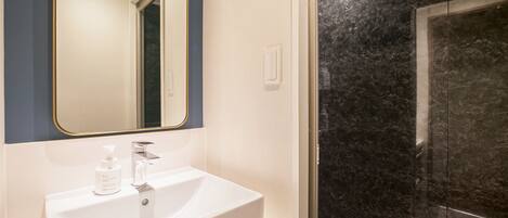 A bathroom with a white sink, a mirror, and a shower with dark marble walls.