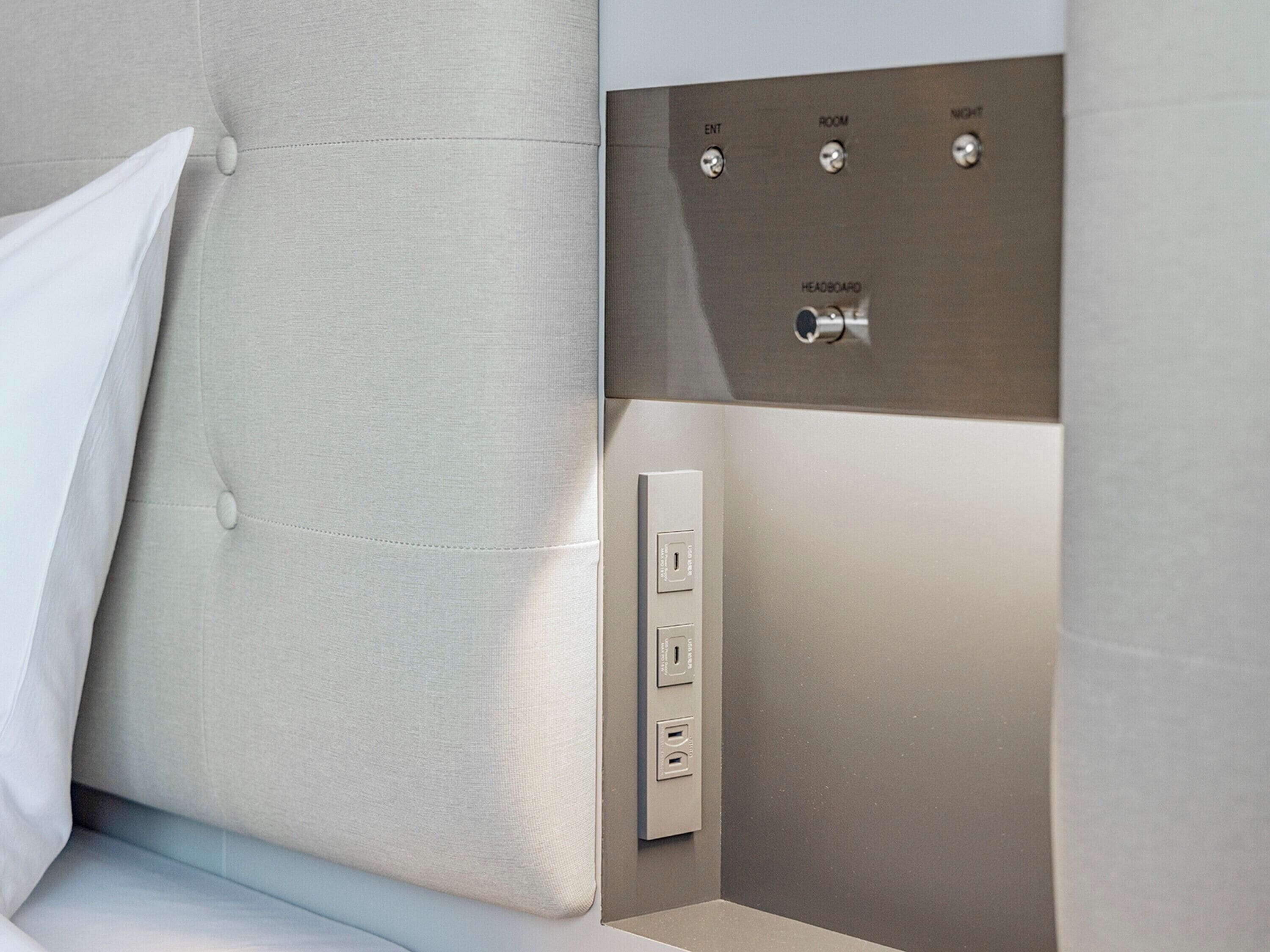 A modern room with a tufted headboard, a control panel with buttons labeled "ENT," "ROOM," "NIGHT," and "HEADBOARD," and a power outlet.