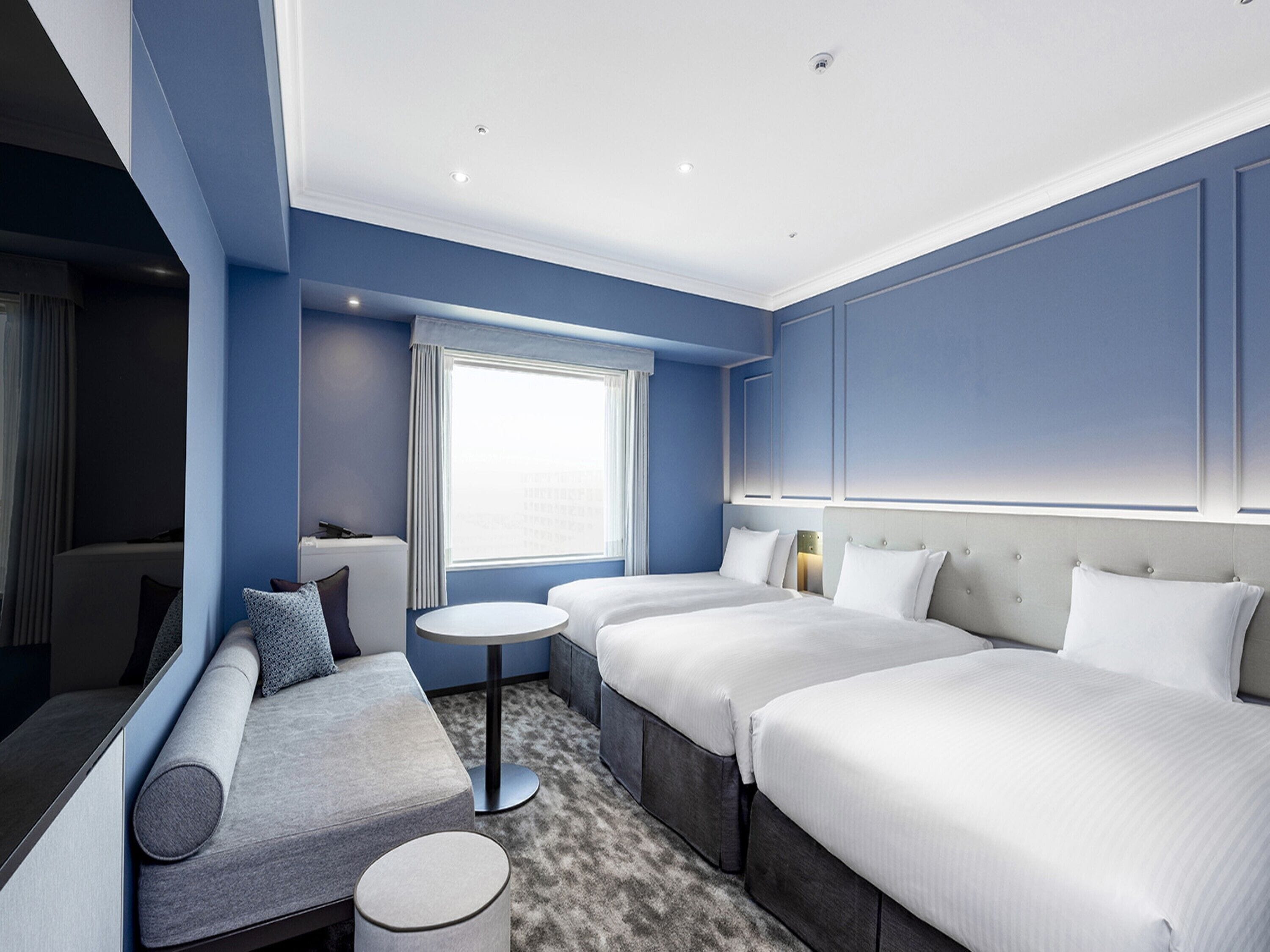 Een moderne hotelkamer met een groot bed, een slaapbank, een klein tafeltje en een raam met gordijnen.