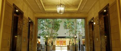 A spacious lobby with marble flooring, a central chandelier, and a view of a restaurant through a glass wall.