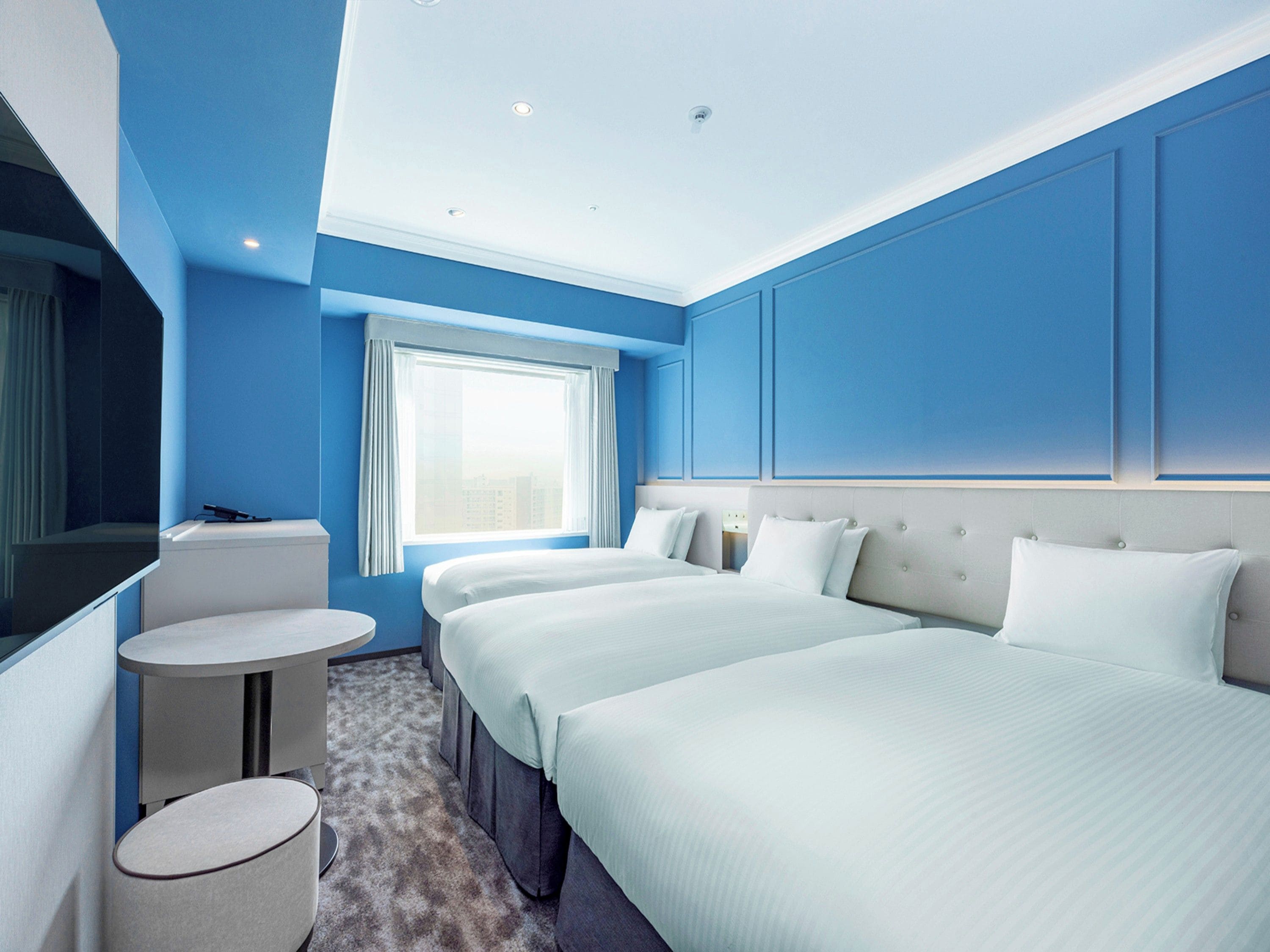 A hotel room with a large bed, a smaller bed, a desk, and a round table.