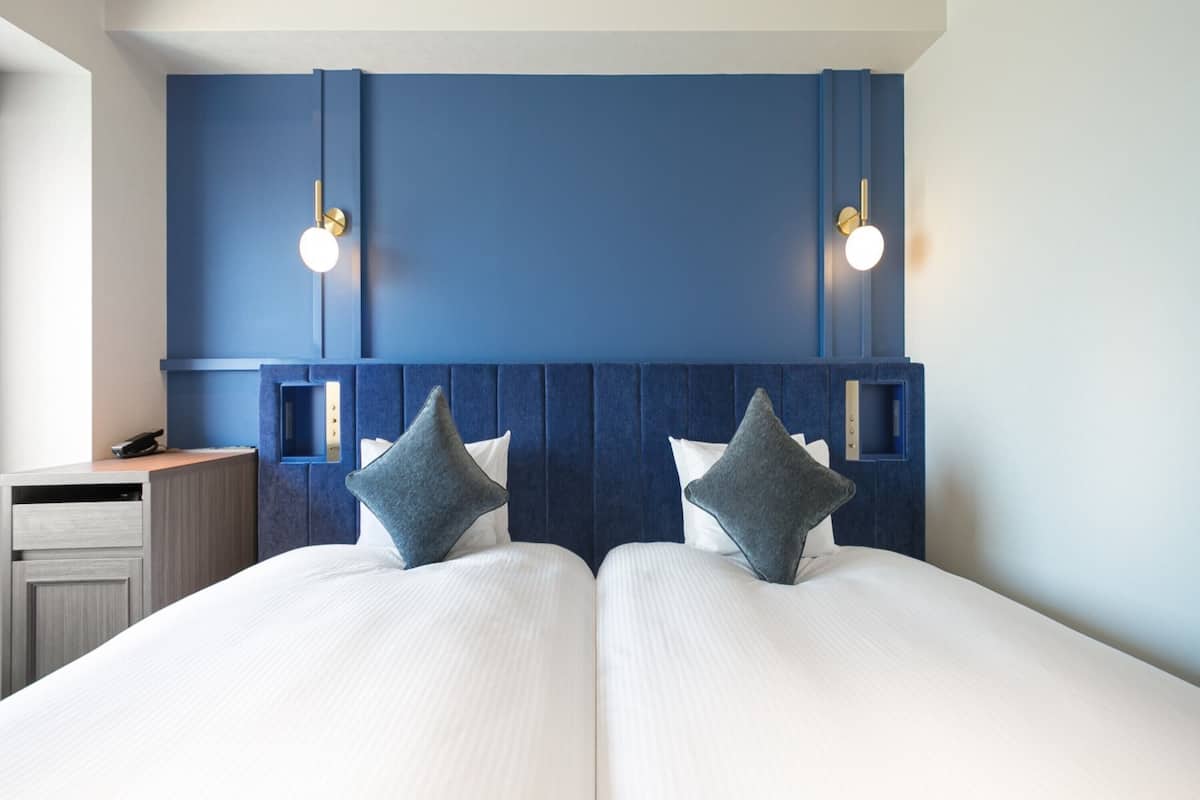 Hotellihuone, jossa on kaksi sänkyä, työpöytä ja sininen tehosteseinä.