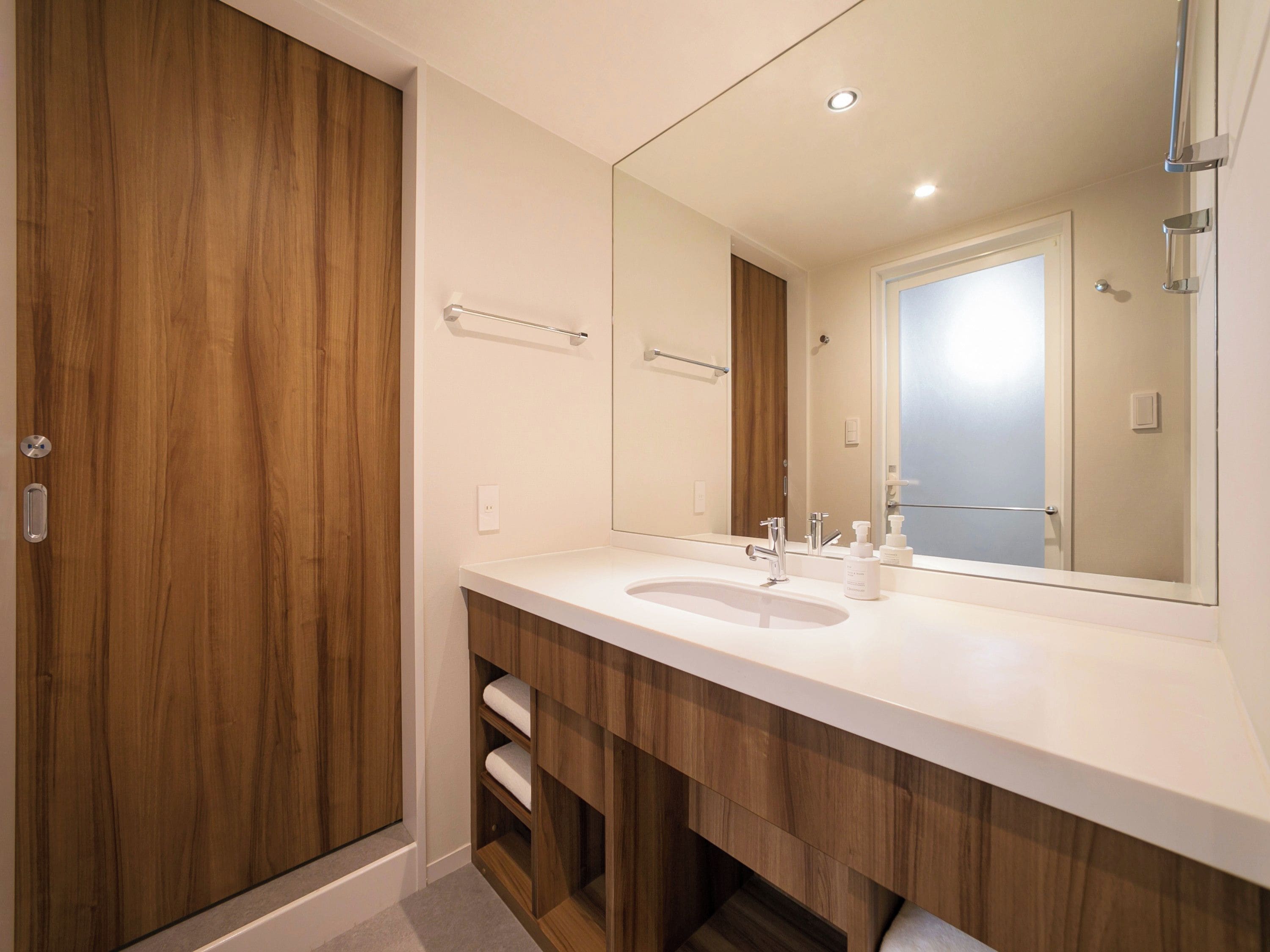 A modern bathroom with a wooden vanity, a large mirror, and a built-in sink.