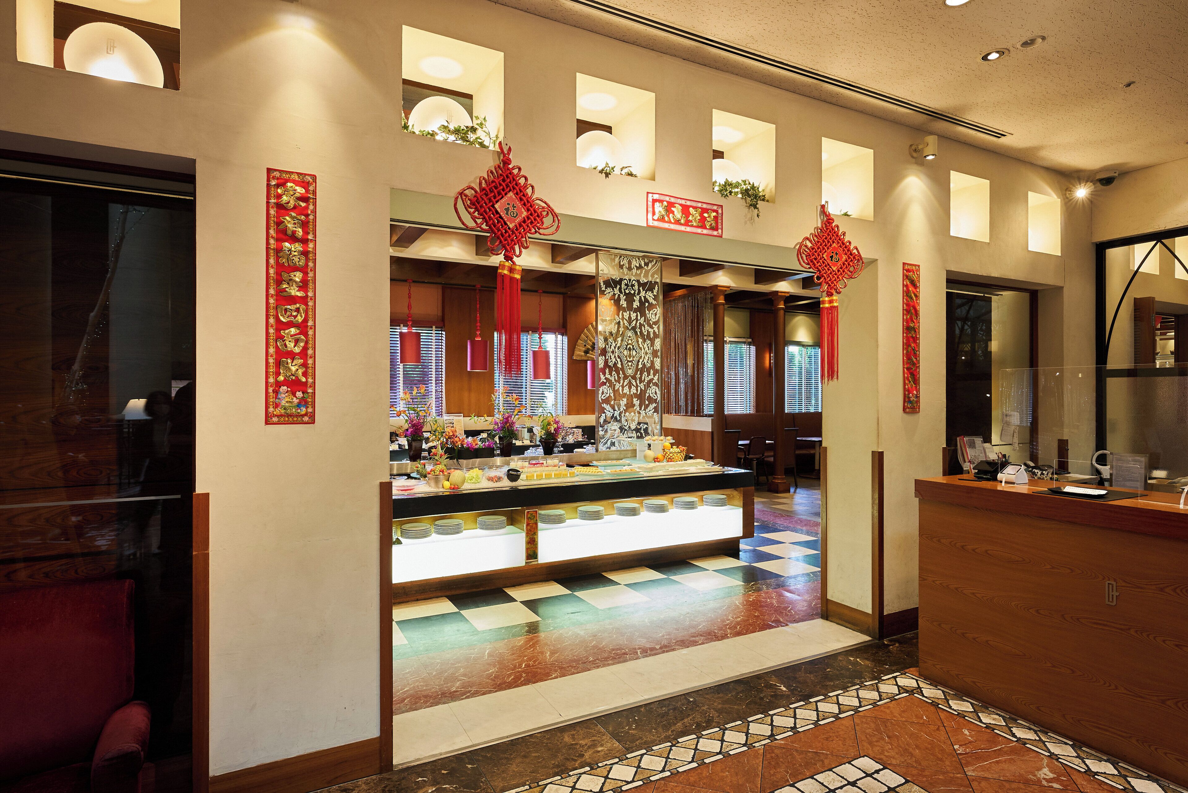 Zona de recepción de un hotel con mostrador de entrada, adornos rojos decorativos y suelo de baldosas.