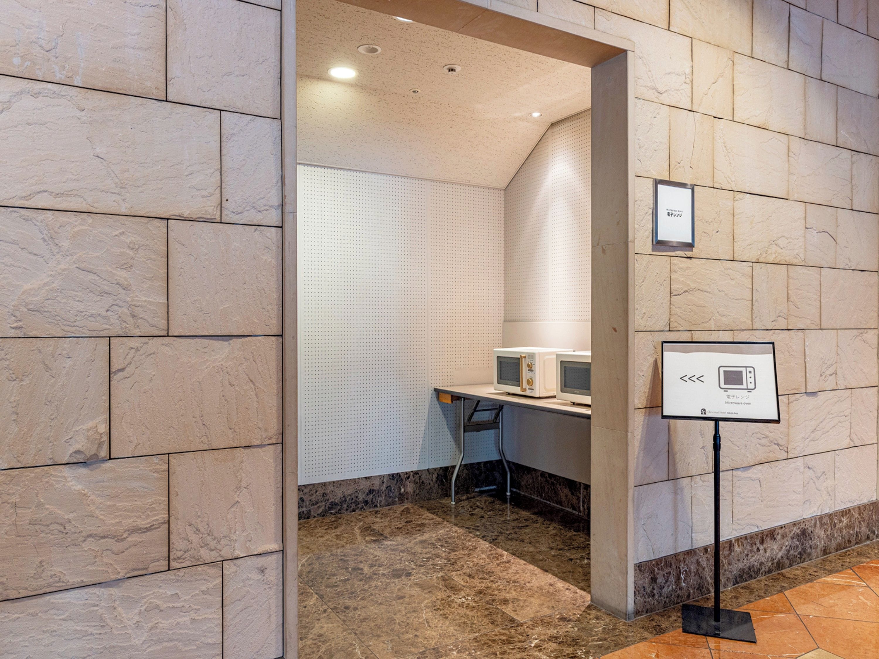 A hotel room with a stone wall, a desk with a computer, and a sign indicating a microwave oven.