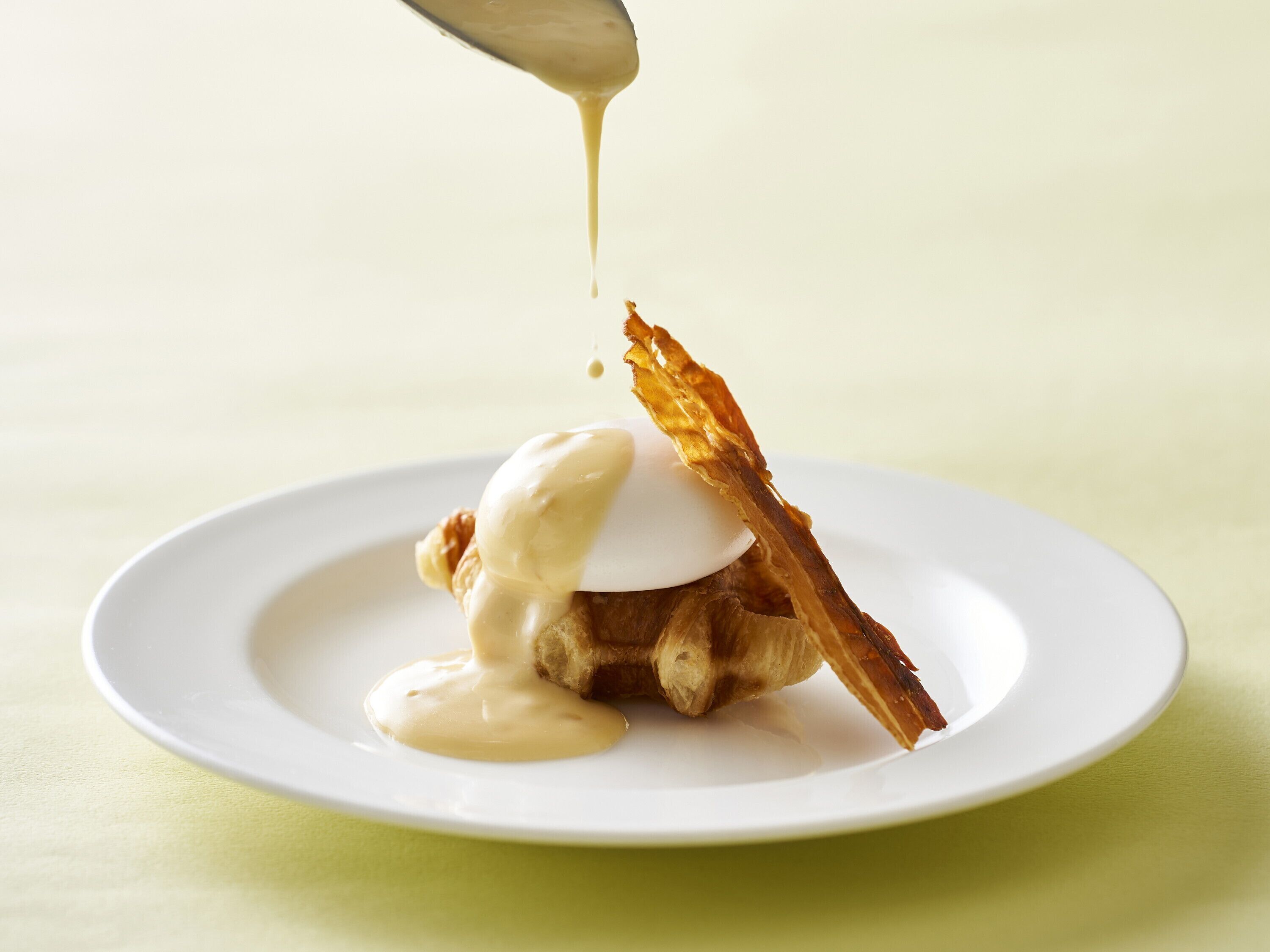 A dessert on a white plate with a spoon pouring sauce over it.