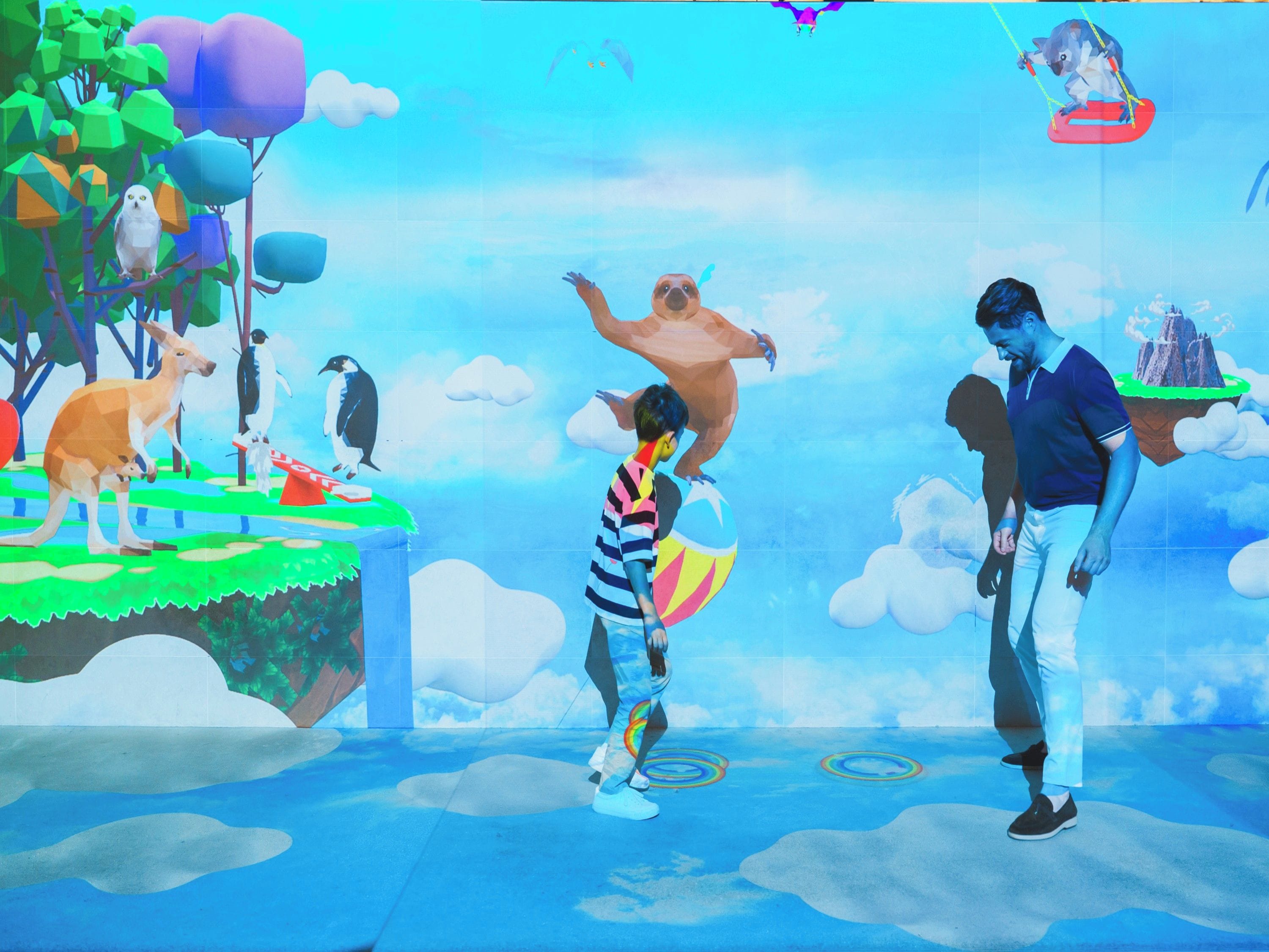 A colorful outdoor scene with a person balancing on a ball, another person holding a child, and a third person standing nearby.
