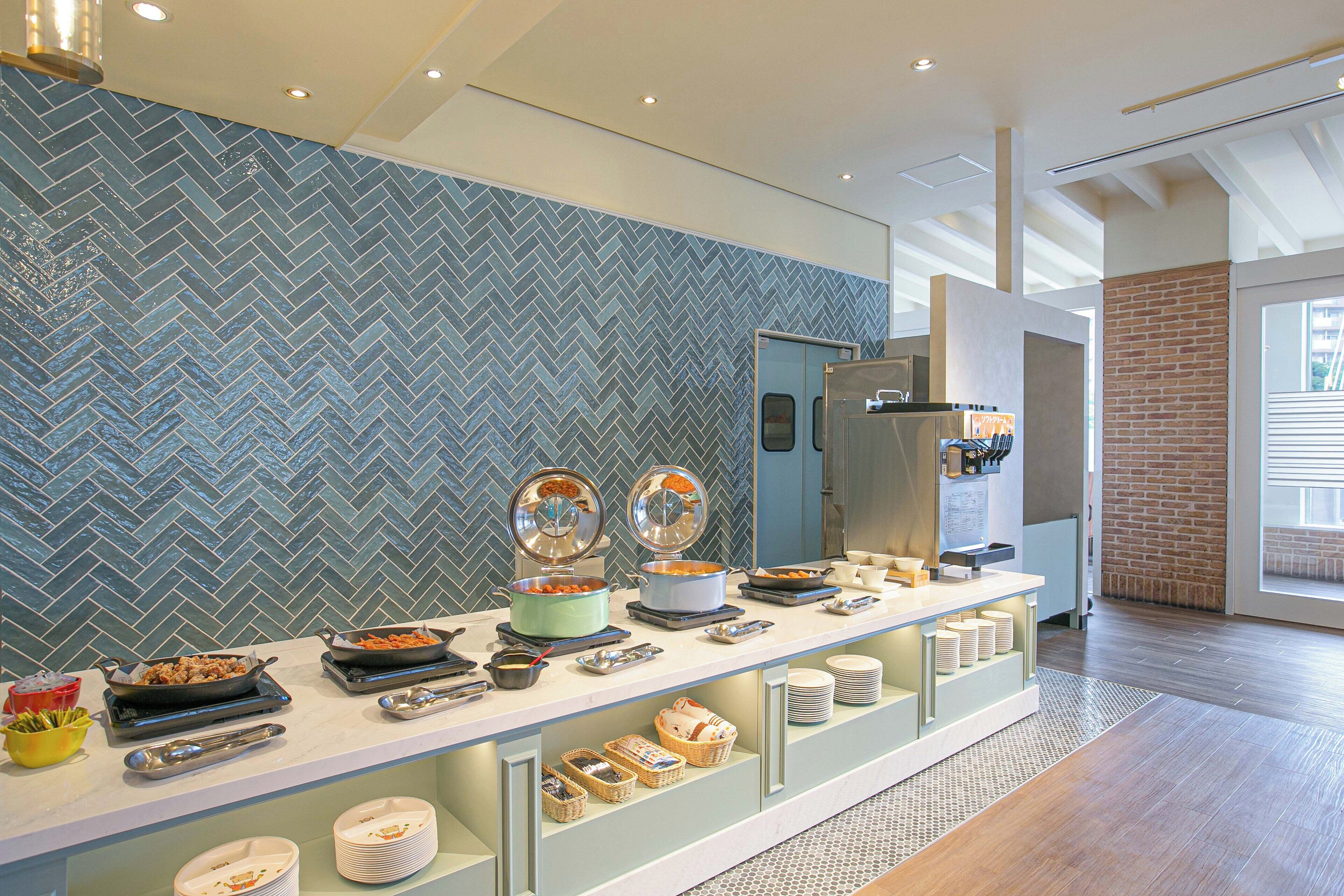 A buffet setup with various dishes and utensils, a herringbone-patterned wall, and a brick accent wall.