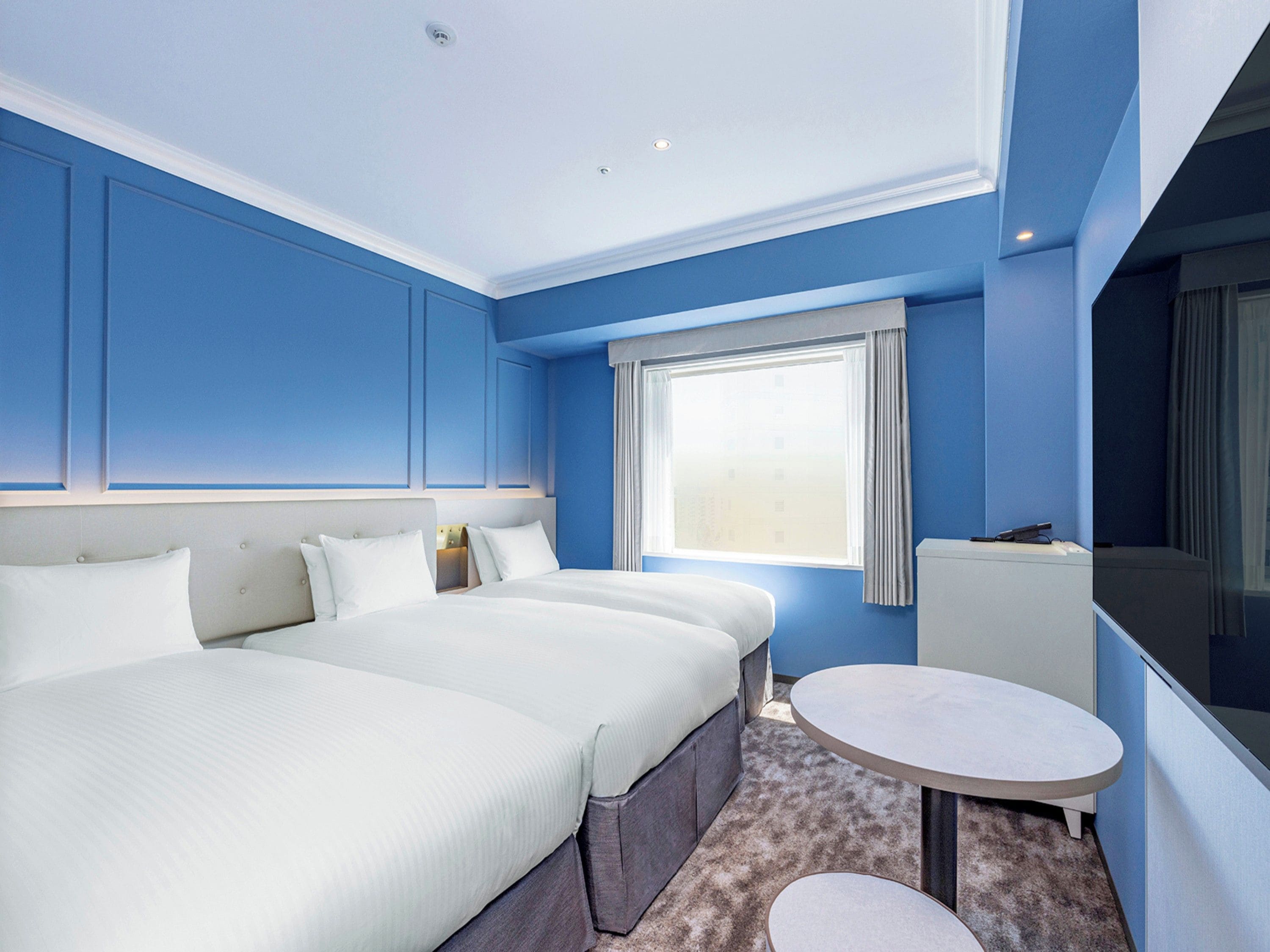 A hotel room with a large bed, a small table, and a window with curtains.