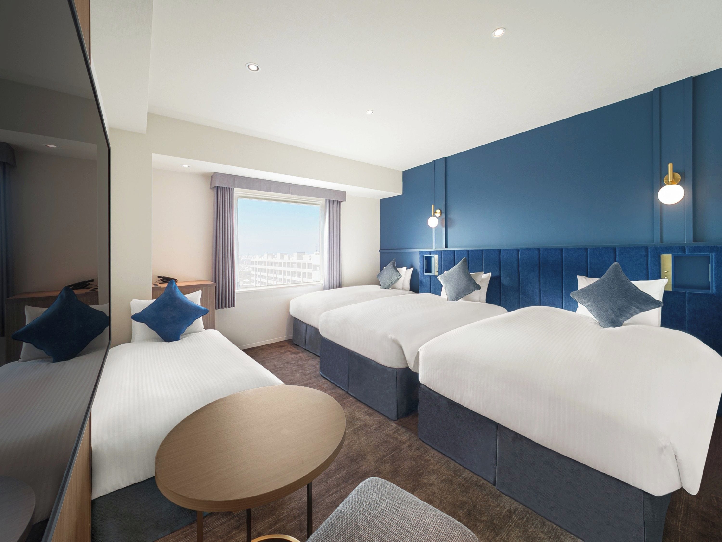 Habitación de hotel con dos camas, una mesita redonda y vista a la ciudad.