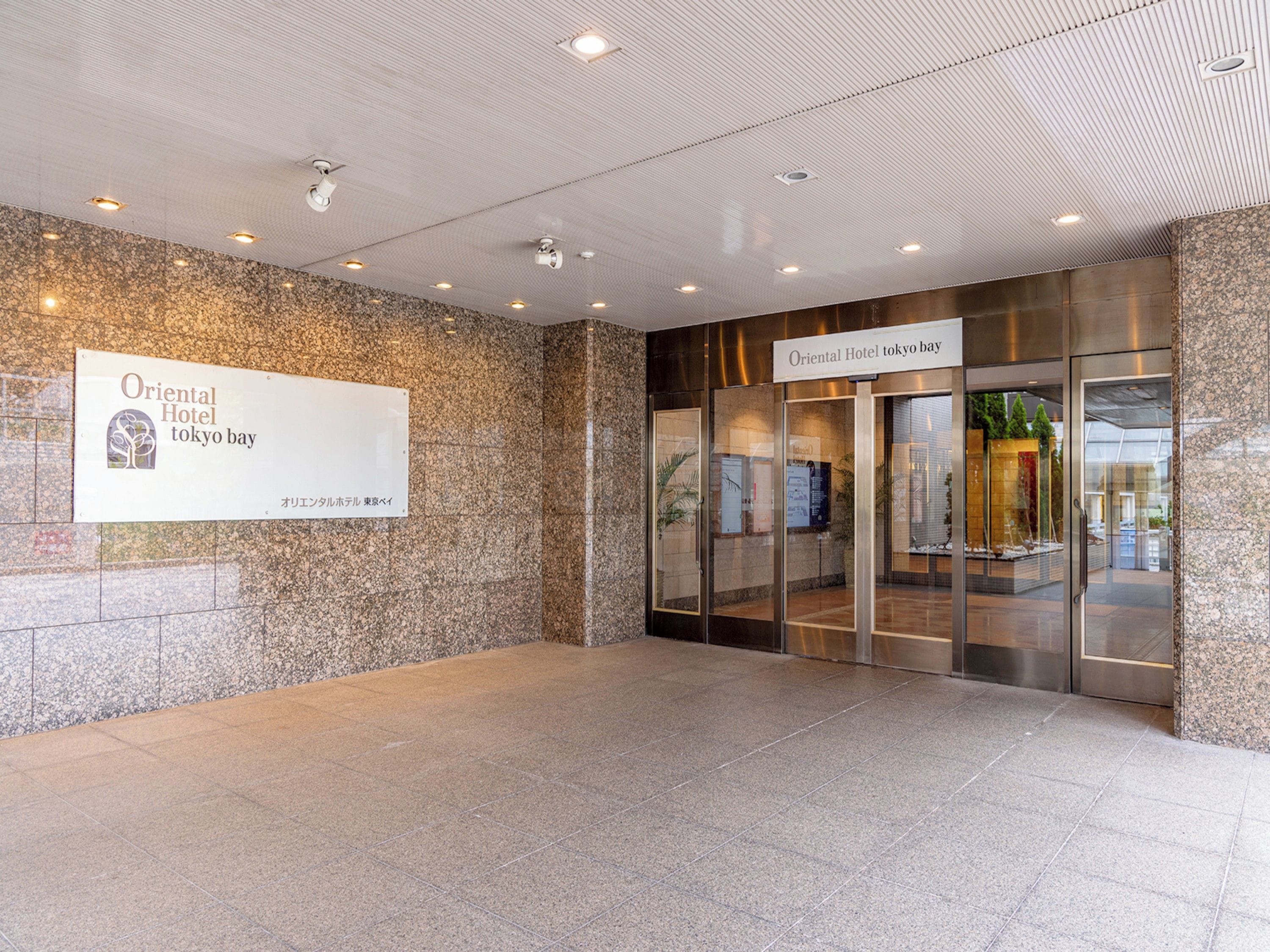 A hotel entrance with a sign reading 'Oriental Hotel Tokyo Bay' and a modern interior with glass doors and a stone wall.