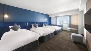 A hotel room with three beds, a small table, and a view of the city.