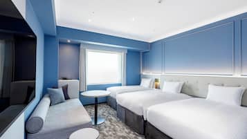 A hotel room with a sofa, two beds, a small table, and a window.