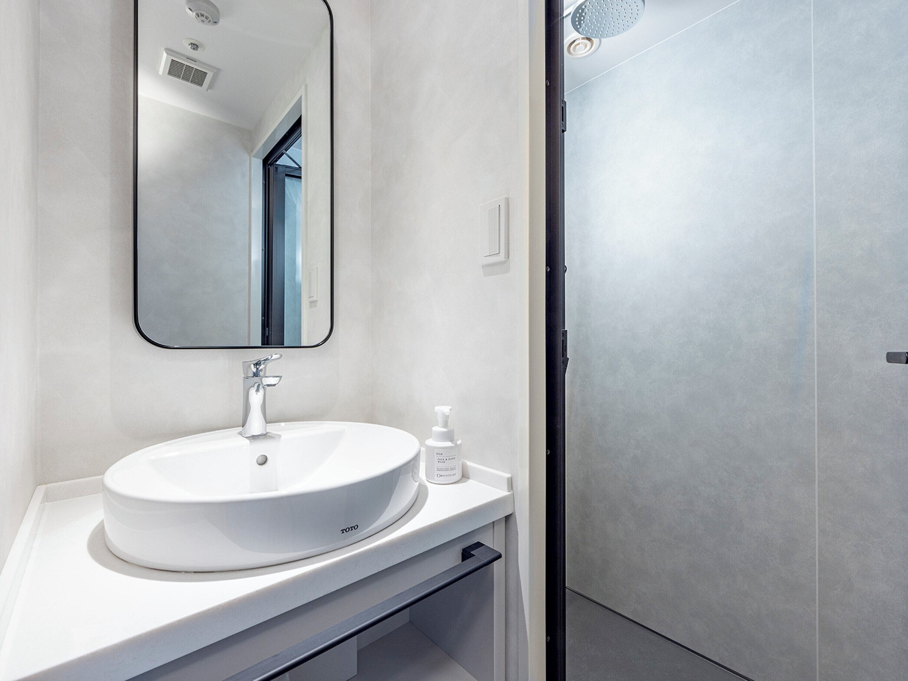 A modern bathroom with a white sink, a mirror, and a shower area.