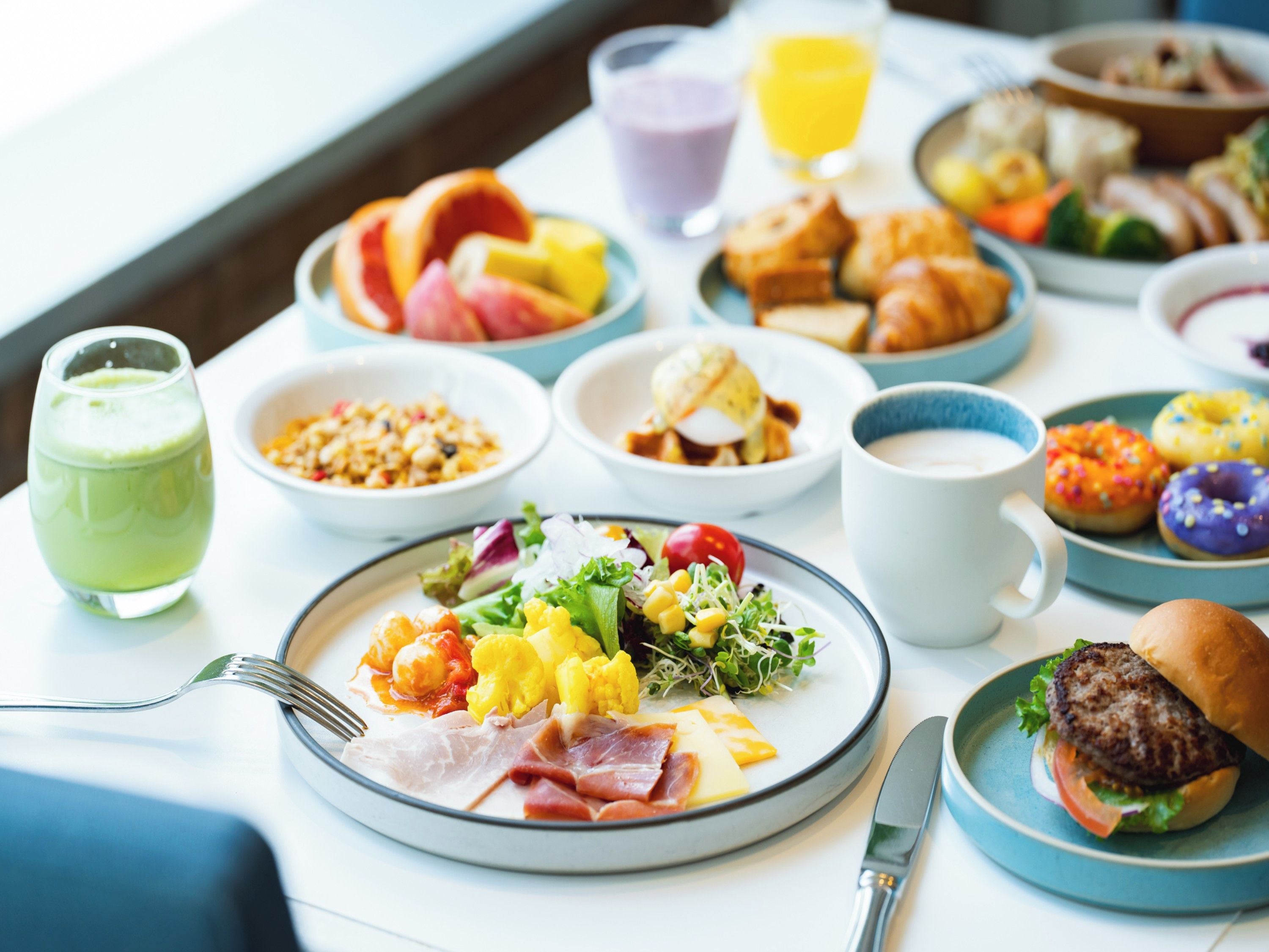 A breakfast buffet with various dishes, including fruits, pastries, and a burger.