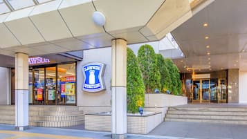 Entrada de hotel con un letrero destacado, fachada con azulejos y un área ajardinada con árboles.