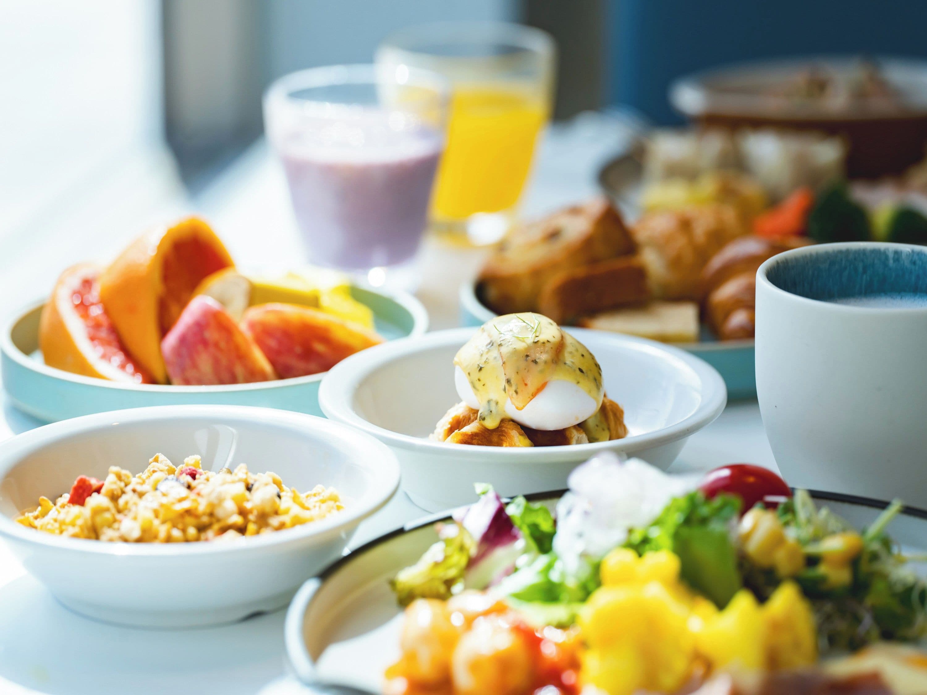 Une variété de plats pour le petit-déjeuner, notamment des œufs, des fruits et des viennoiseries, sont disposés sur une table.