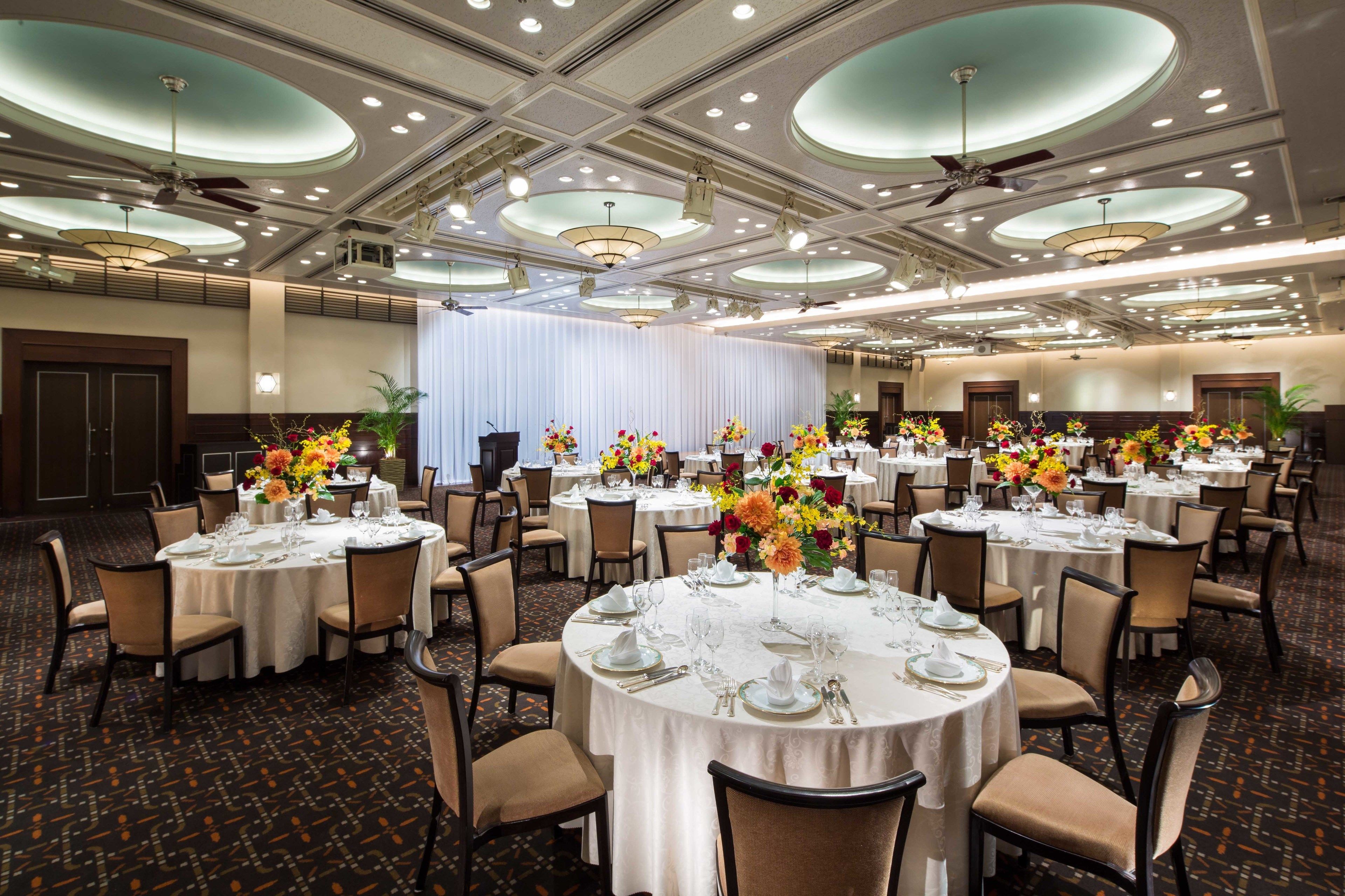 Une salle de banquet avec des tables rondes dressées pour le repas, agrémentées de nappes blanches et de compositions florales.