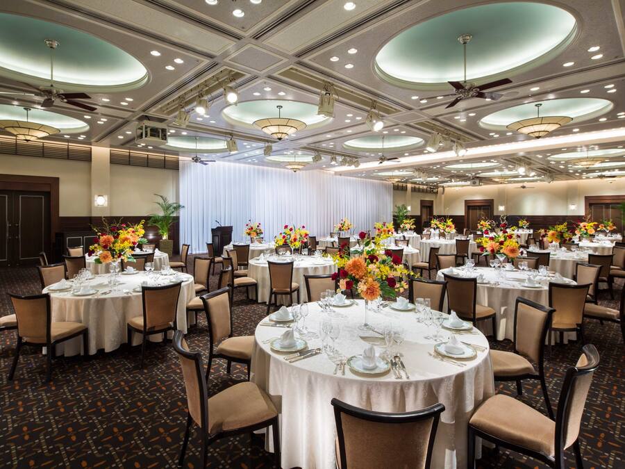 A banquet hall with round tables set for dining, featuring white tablecloths and floral centerpieces.