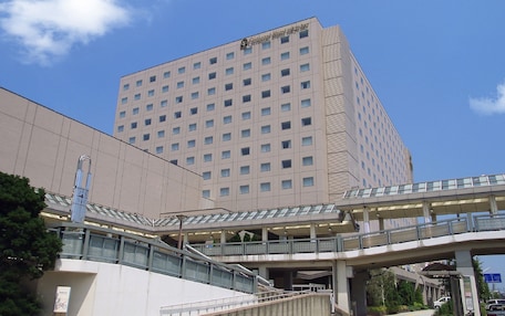 A multi-story hotel with a modern design, featuring a prominent entrance and a pedestrian overpass.