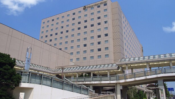 Ein mehrstöckiges Hotel mit modernem Design, das eine markante Eingangshalle und eine Fußgängerbrücke aufweist.