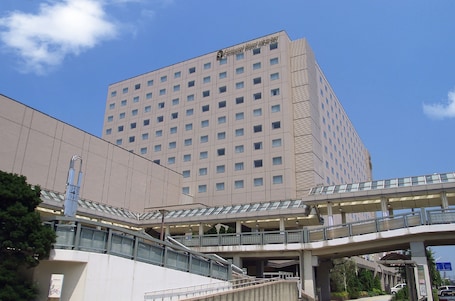 A multi-story hotel with a modern design, featuring a prominent entrance and a pedestrian overpass.
