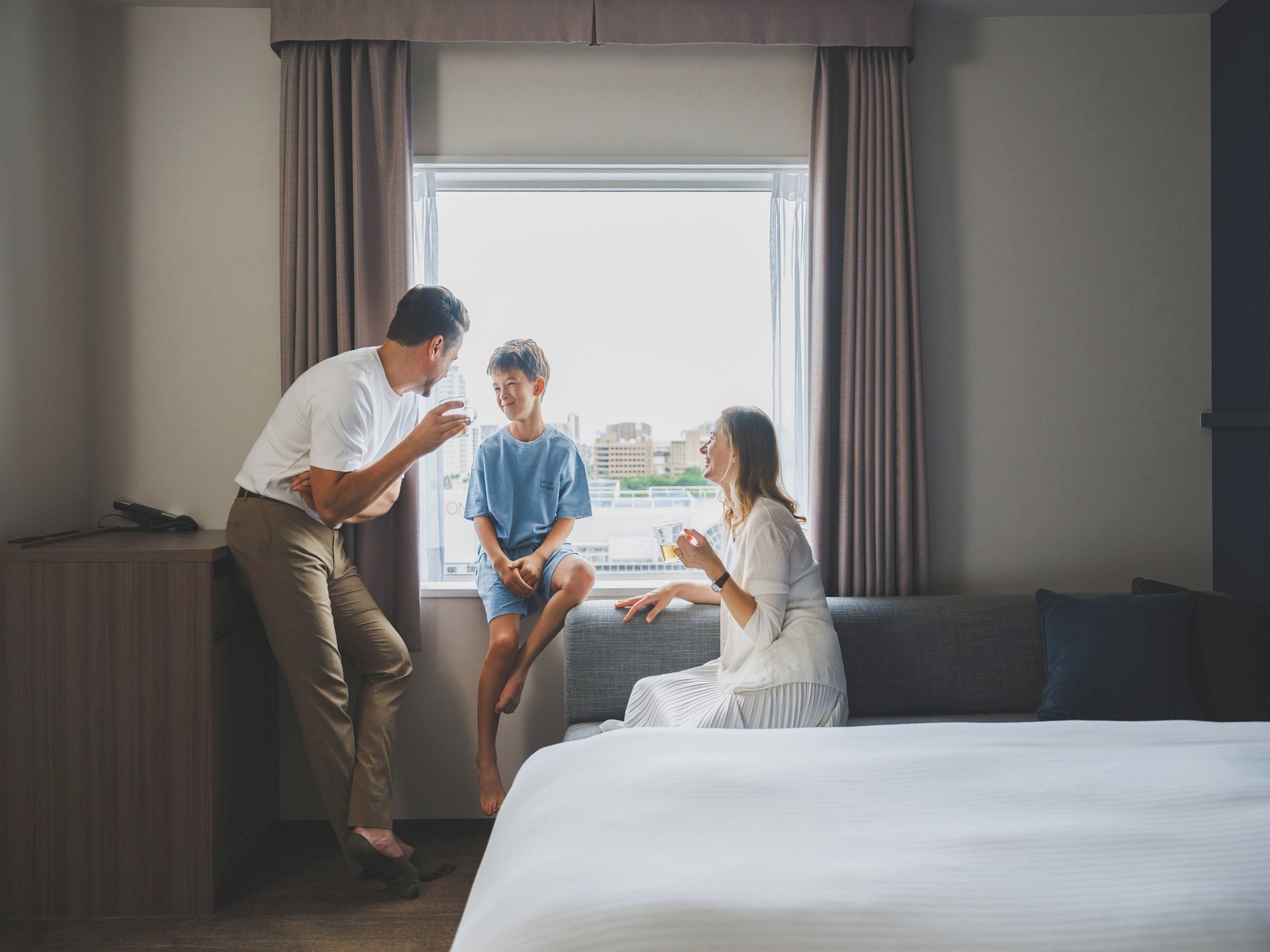 A hotel room with a bed, a window with curtains, and a city view.