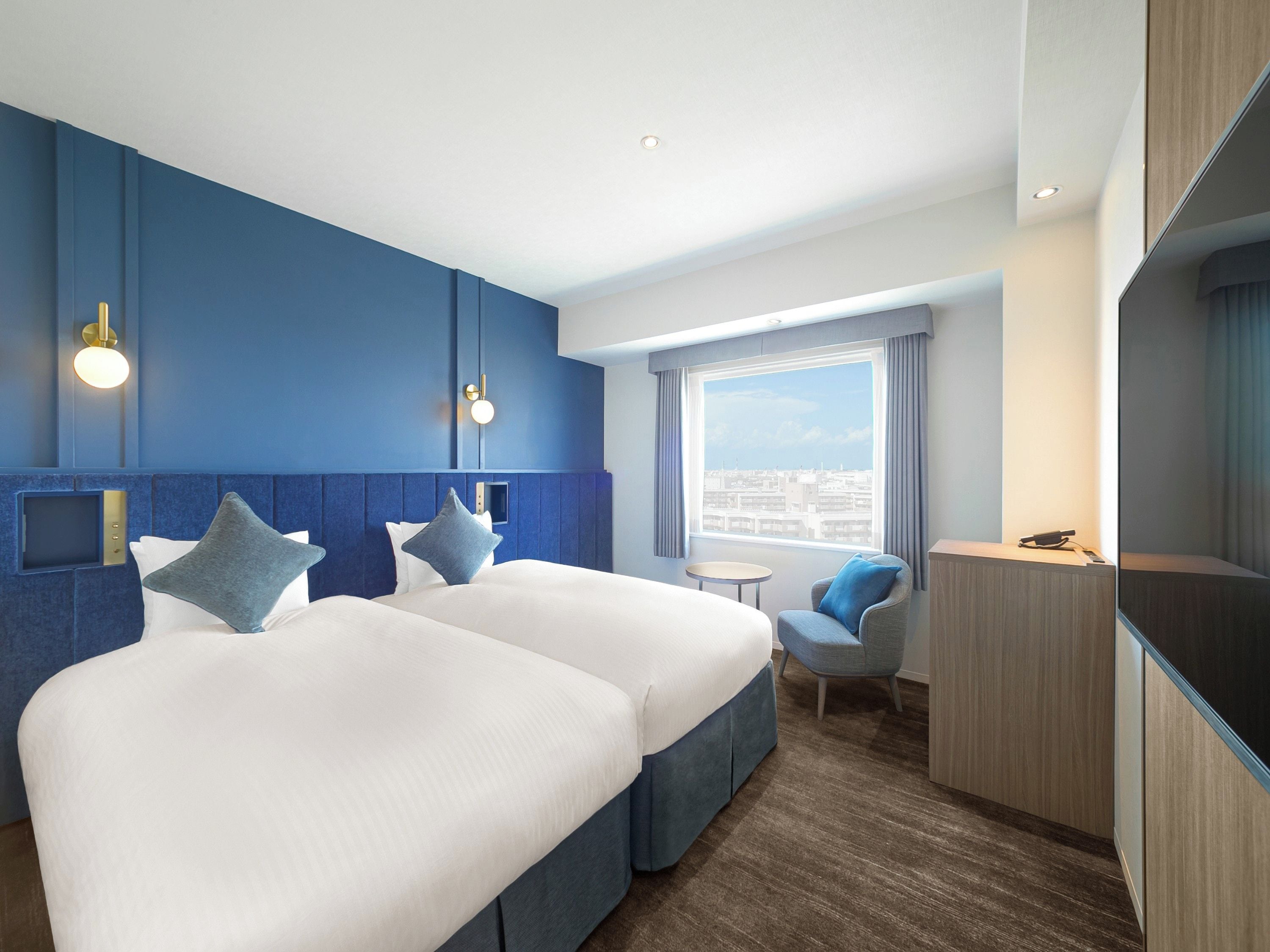 A hotel room with a large bed, a seating area, a desk, and a city view.
