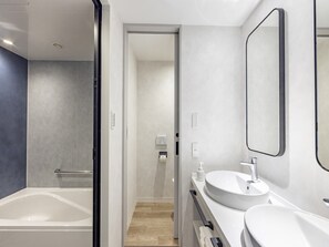 A modern bathroom with a bathtub, two sinks, and a large mirror.