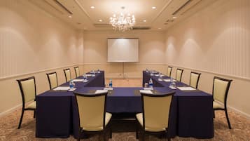 A conference room with a long table, chairs, a projector screen, and a chandelier.