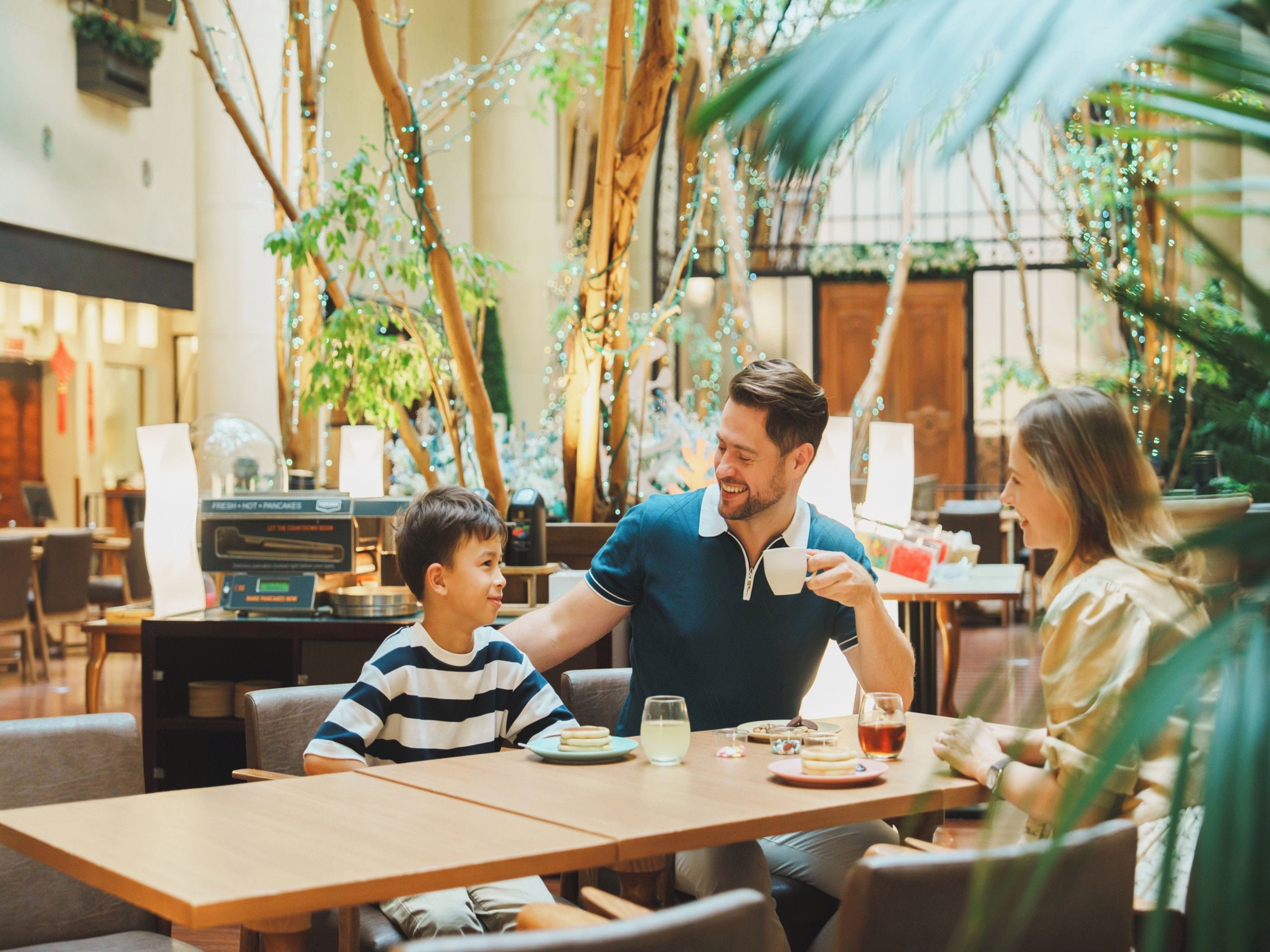 A family dining at a table with a view of indoor plants and string lights.