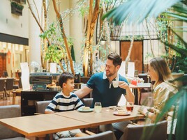 Una familia cenando en una mesa con vistas a plantas de interior y luces colgantes.