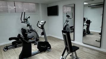 Un gimnasio con equipo de ejercicio, televisión y espejos.
