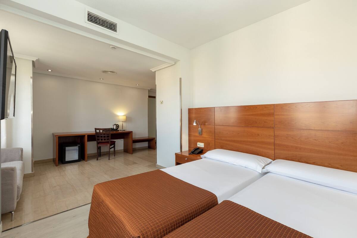 Quarto de hotel com duas camas, uma escrivaninha e uma cadeira.