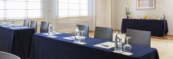 Un salón de conferencias con mesas dispuestas para una reunión, equipado con botellas de agua, vasos y blocs de notas.