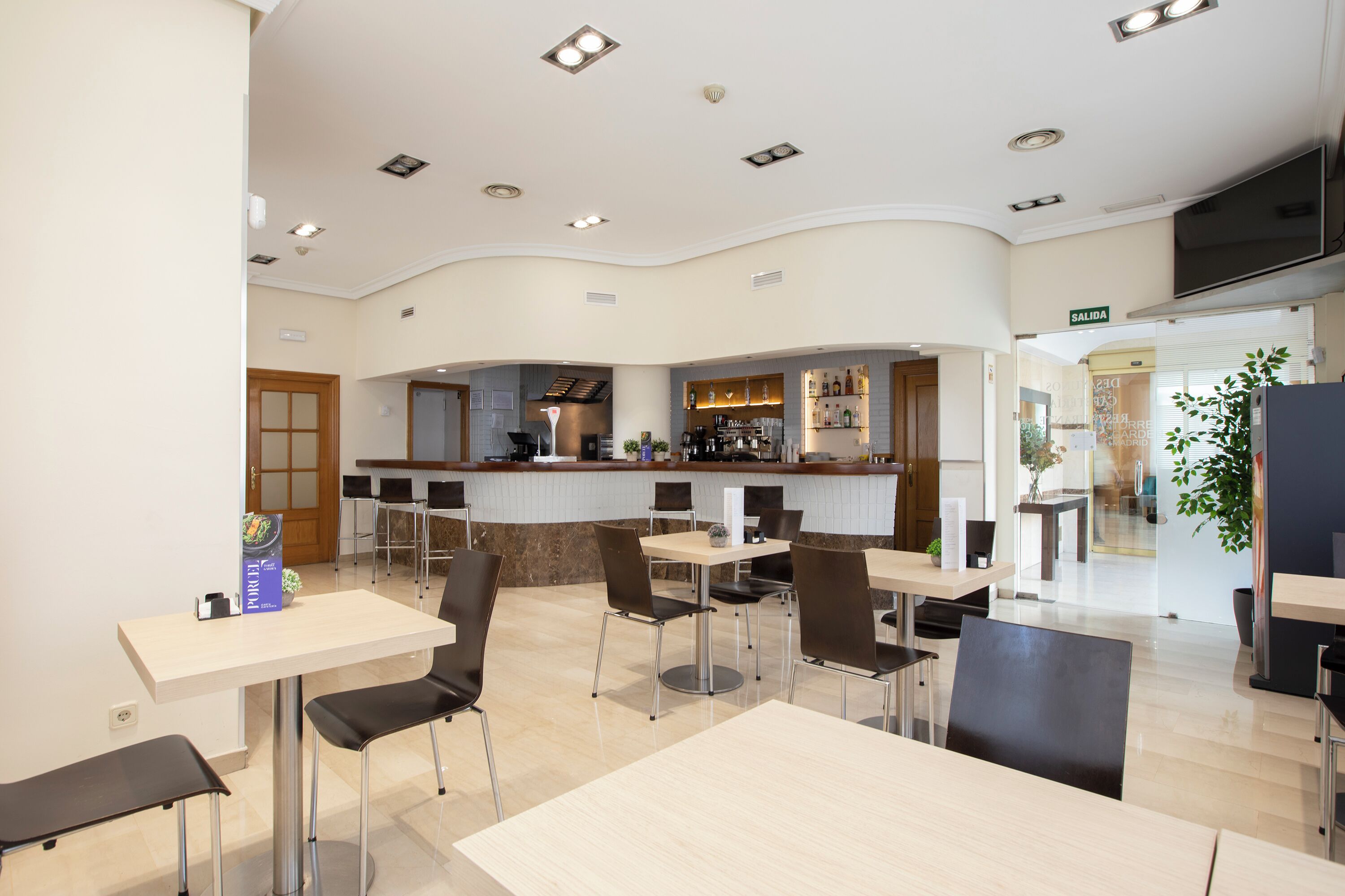 Un restaurant moderne doté d’un plafond incurvé, de nombreuses tables et chaises, d’un bar et d’un panneau indiquant la sortie.