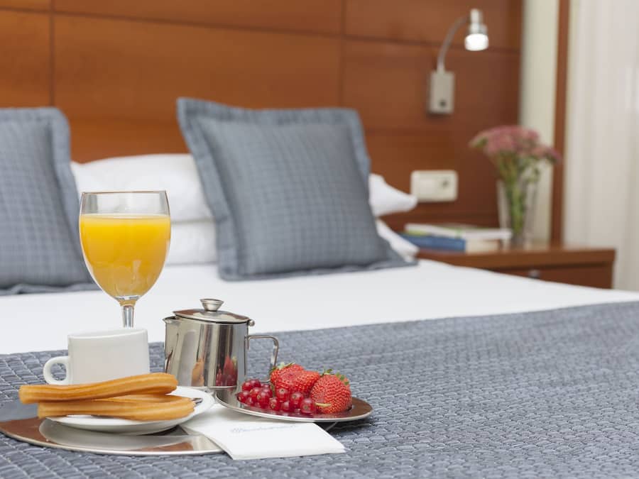 Desayuno en la cama con vaso de jugo de naranja, taza, churros y fresas.