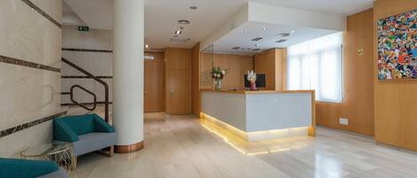 A modern lobby with a reception desk, seating area, and a staircase.