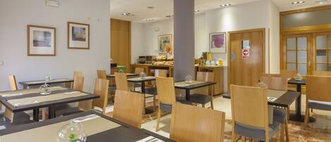 Un'area ristorazione in un hotel con diversi tavoli e sedie, un angolo caffè e opere d'arte appese alle pareti.