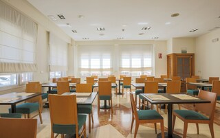 A spacious dining area with multiple tables and chairs, large windows, and a wooden cabinet labeled 'SALIDA'.