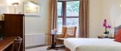 A hotel room with a bed, a desk, a chair, and a window with curtains.