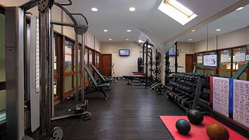 A gym with various exercise equipment, a mirrored wall, and a red mat with exercise balls.