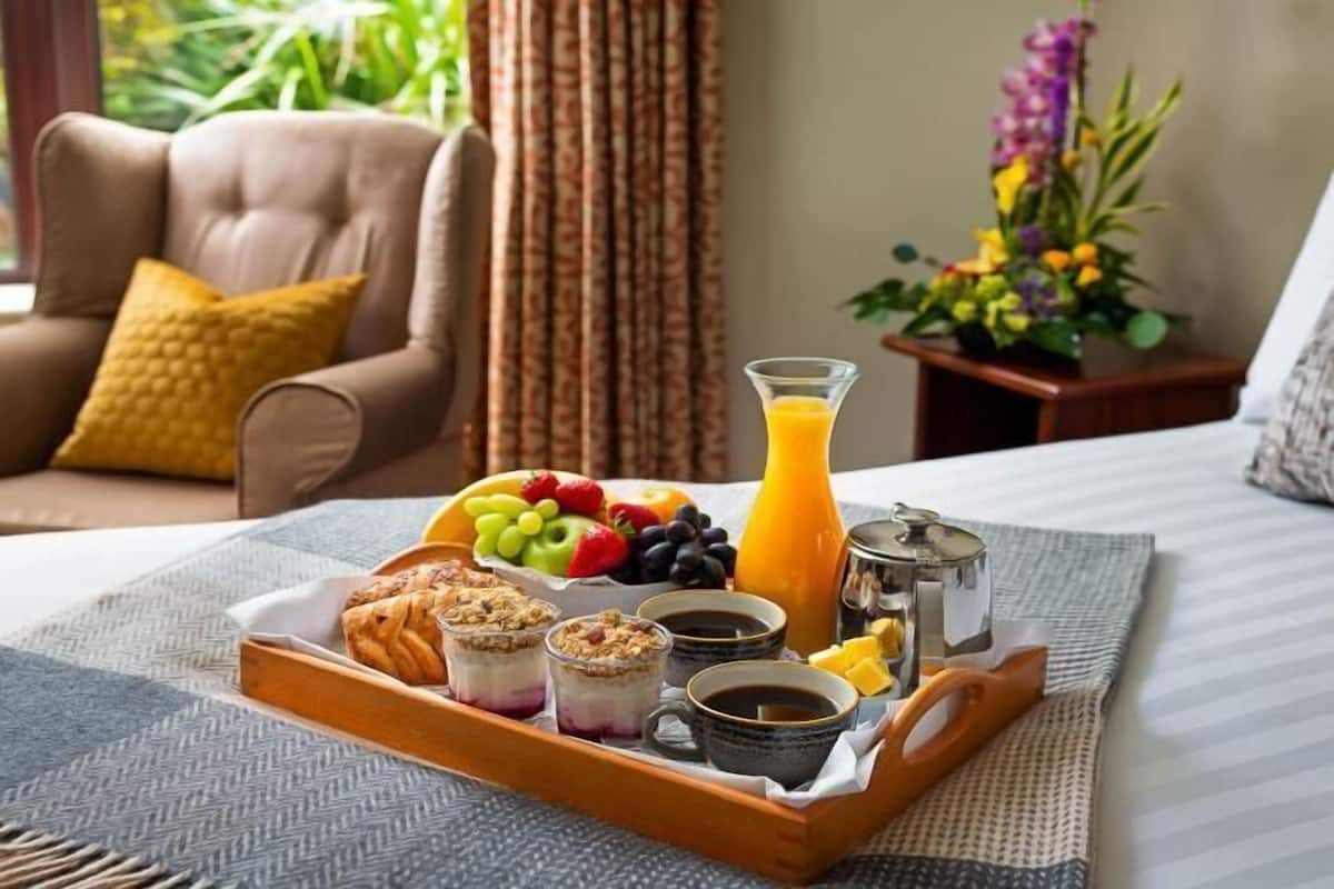 A breakfast tray with fruits, pastries, coffee, and juice on a bed.