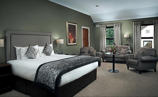 A hotel room with a large bed, two armchairs, a sofa, a coffee table, and a painting on the wall. - Oranmore Lodge Hotel Galway (Oranmore)